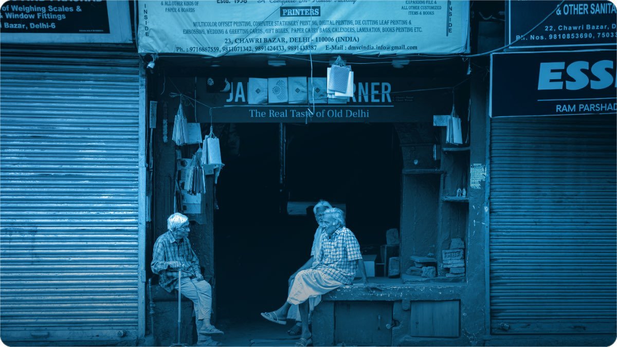 Two older men sitting and talking in the open doorway of a shop in an old bazaar street.