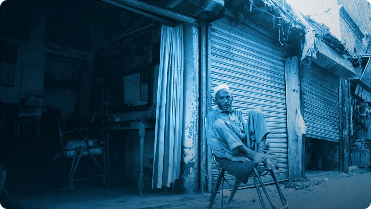 Ek dukandar khamosh bazaar mein apni band shutter ke bahar kursi par baitha hai.