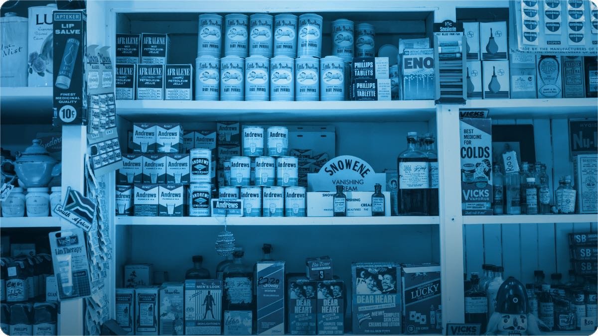 A shop owner arranging new items on a wooden display shelf inside his store.