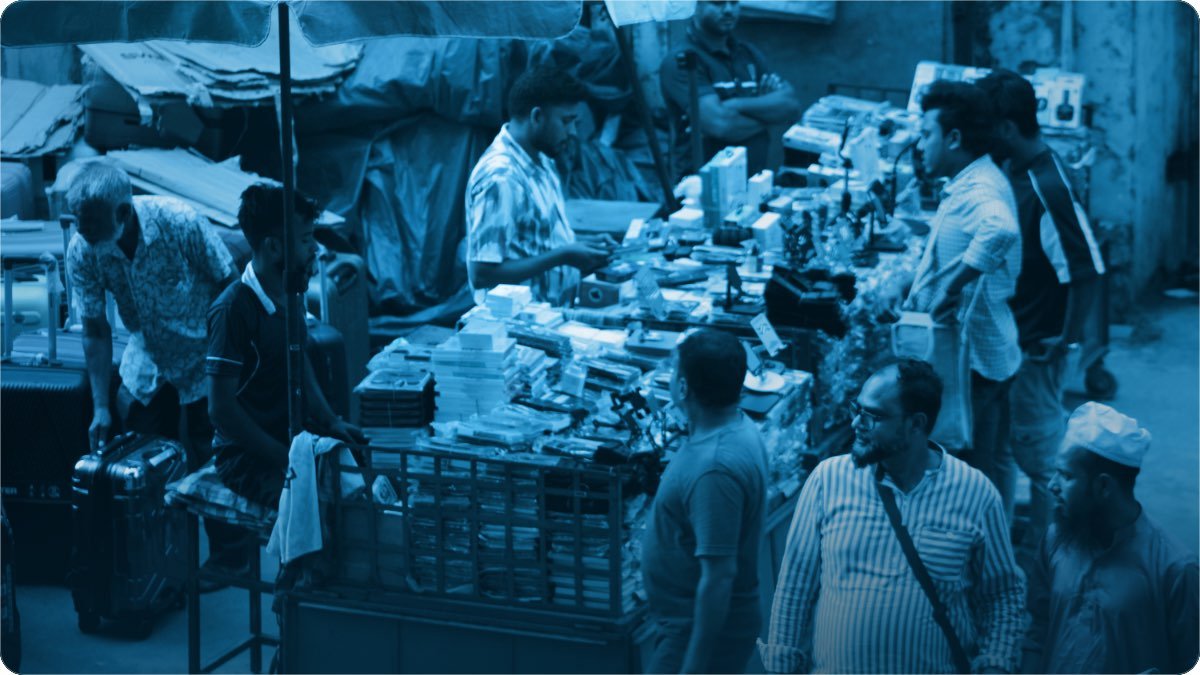 Sarak kinare ek stall par electronics aur ghar ka saman laga hua, gird customers ka hujoom.