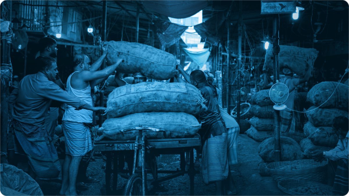Log bhaari boriyan thele par chadha rahe hain, thok mandi ki gali nange bulbon se roshan hai.