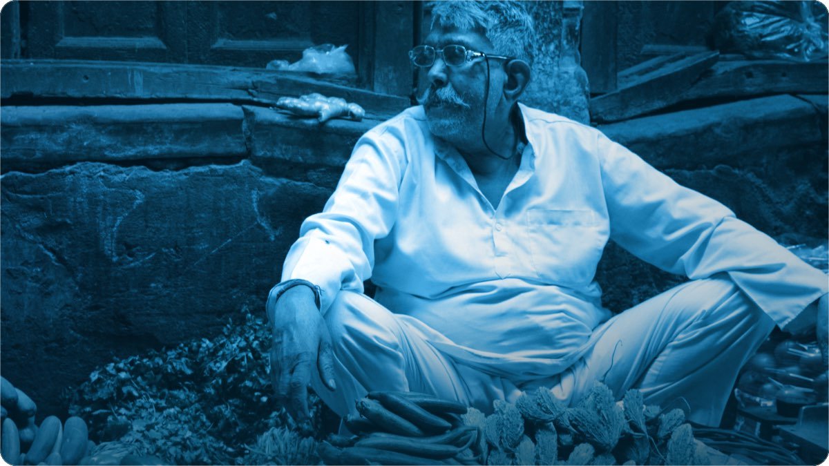 Umar rasida sabzi farosh kurta pehne apni sabzi ke paas baitha hai, sochta hua doosri taraf dekh raha hai.