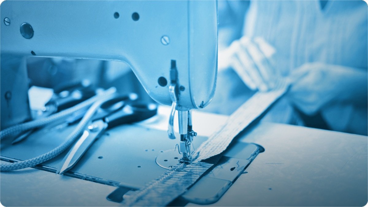 A working sewing machine stitching a strip of fabric in a small workshop.
