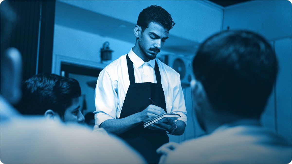 A shopkeeper writing an order in his notebook while customers wait.