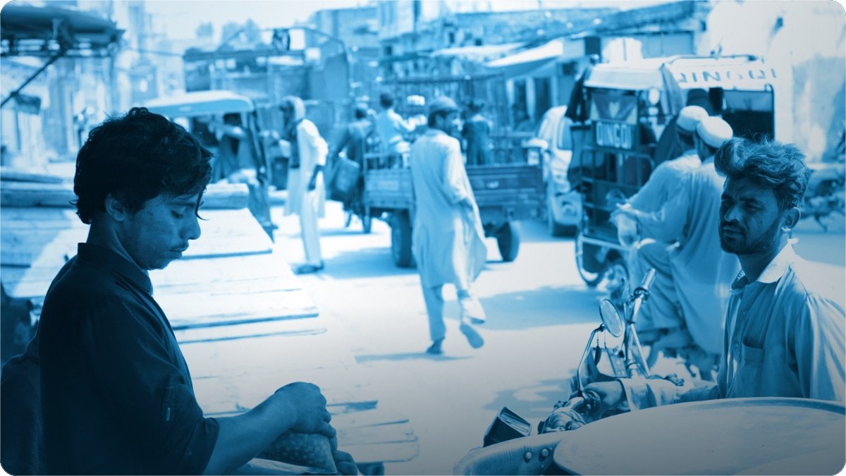 Masroof bazaar mein apne thele par khara dukandar, aur us ke barabar motorcycle par khara ek aadmi.