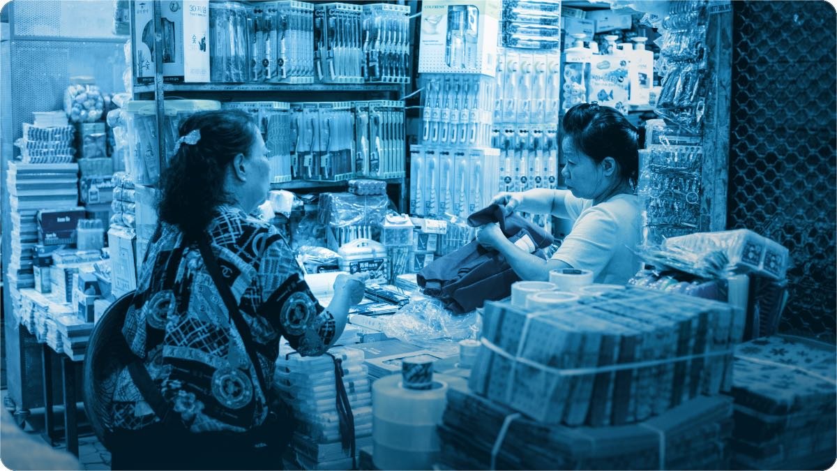 A shopkeeper leaning on his counter, listening to a customer at the shop door.