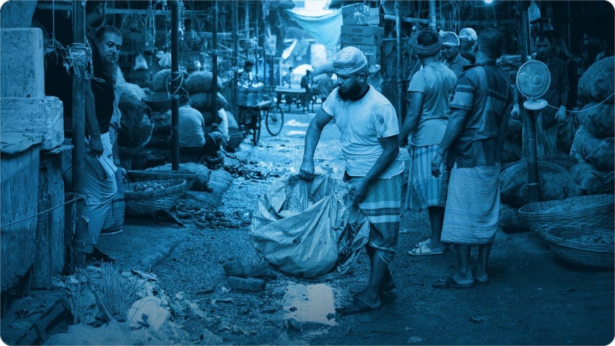 Ek aadmi sabzi mandi ki bheer bhari galli mein bhaari bora ghaseet raha hai.