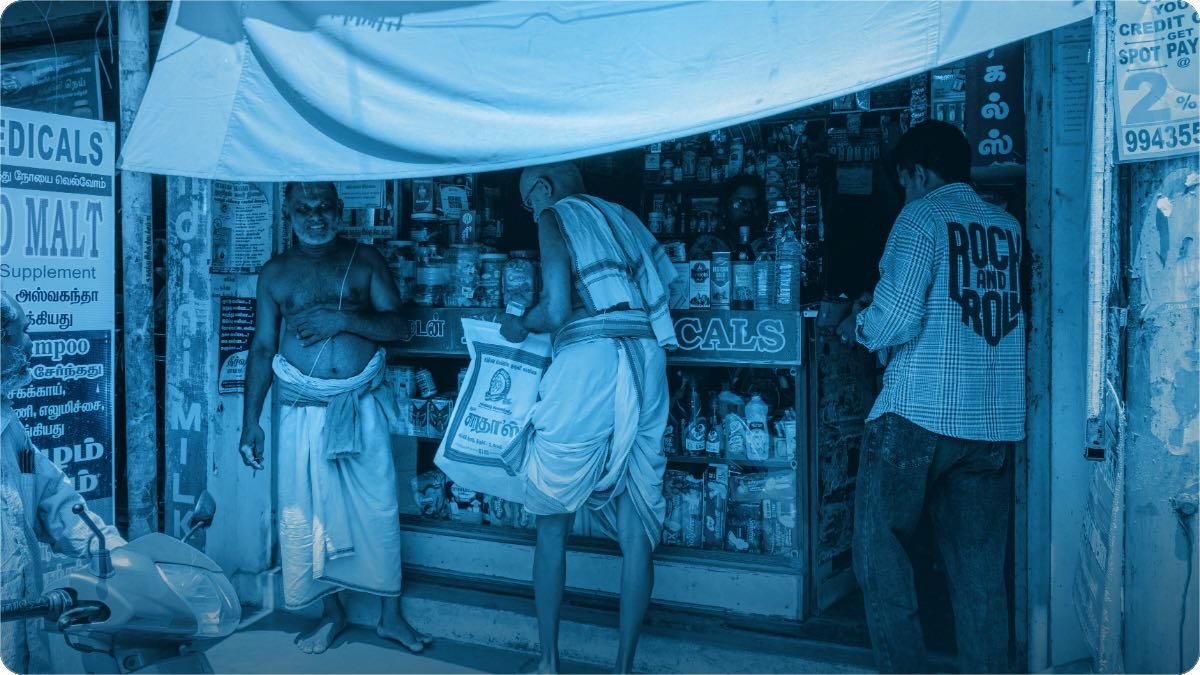 Customers standing at the counter of a small street shop while one man serves them.
