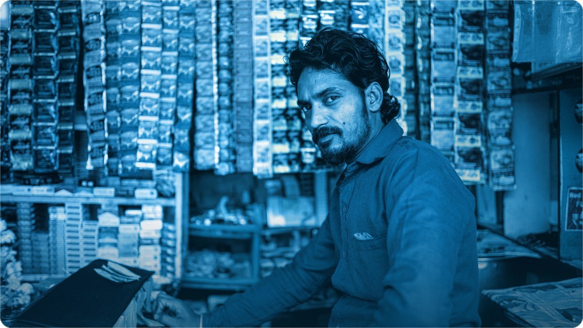 Dukandar apne counter se nazar uthata hai, chhoti dukan ki deewaron par sachet aur packeton ki lambi lariyan.