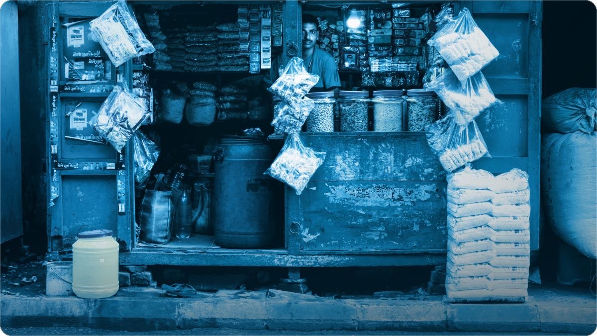 A small shop stocked with jars, sacks and hanging packets, the shopkeeper standing behind the counter.