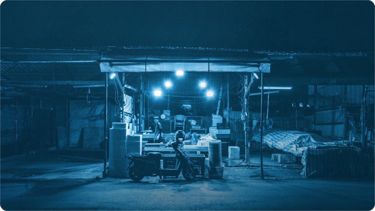 A street shop in South Asia lit up after dark, its lamps the only light on the road.