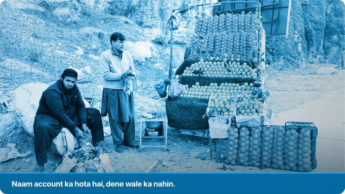 Two roadside sellers beside a stall of fruit and crates on a South Asian highway.