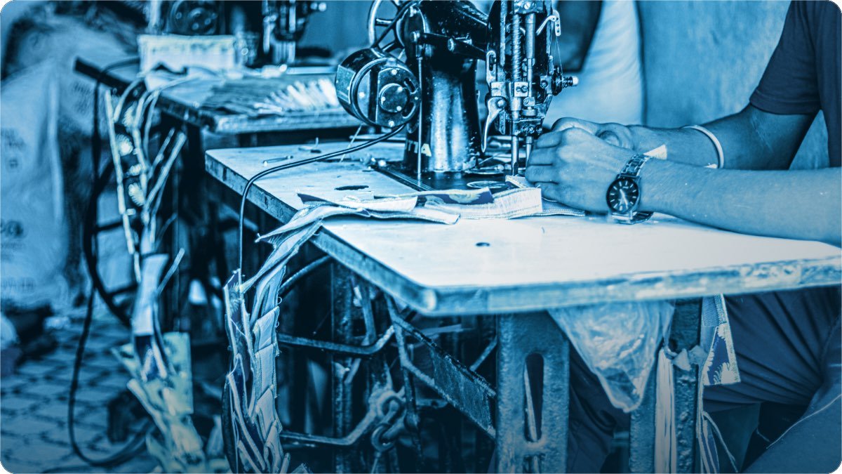 A tailor guiding fabric under the needle of an old sewing machine at his workbench.