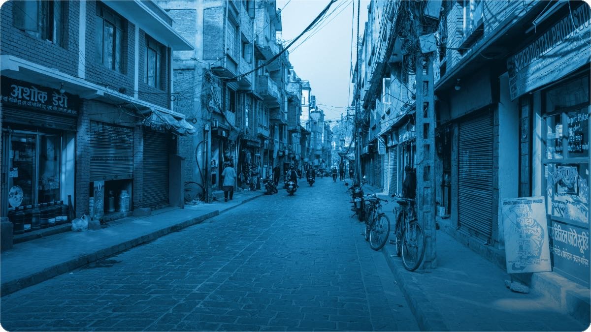 Choti dukanon wali tang gali, lohe ke shutter, cyclein aur hath se likhe hue board.