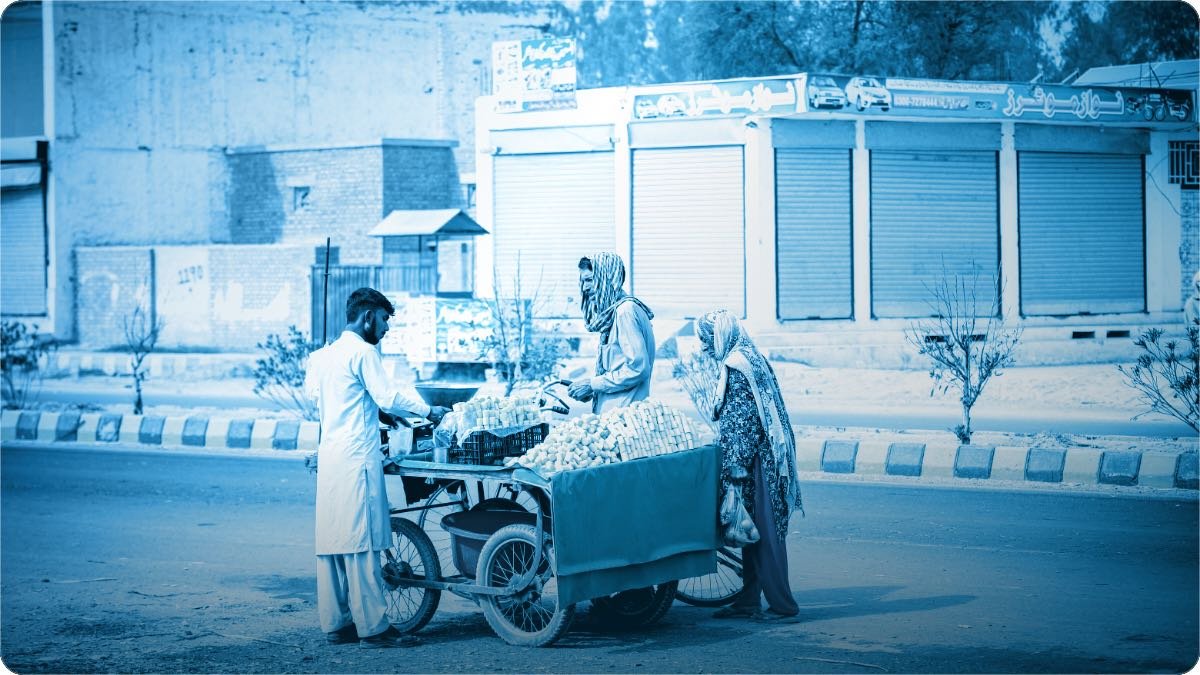 Pakistan mein rehri wala do customeron ko saman de raha hai, peechay Urdu bordon wali band dukanein.