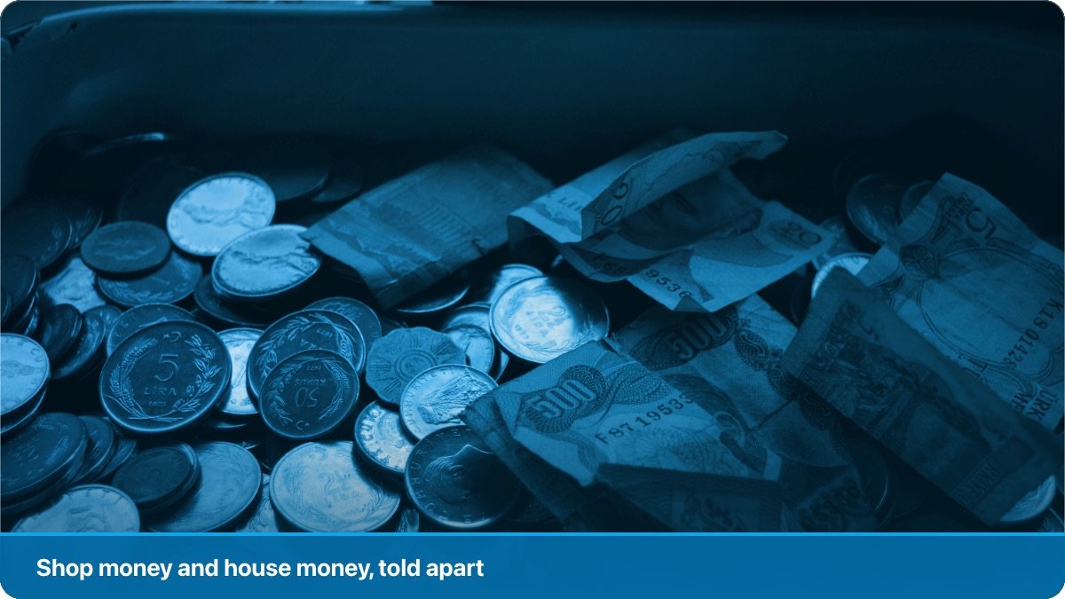 A cash box open on a shop counter beside a notebook and a pen.