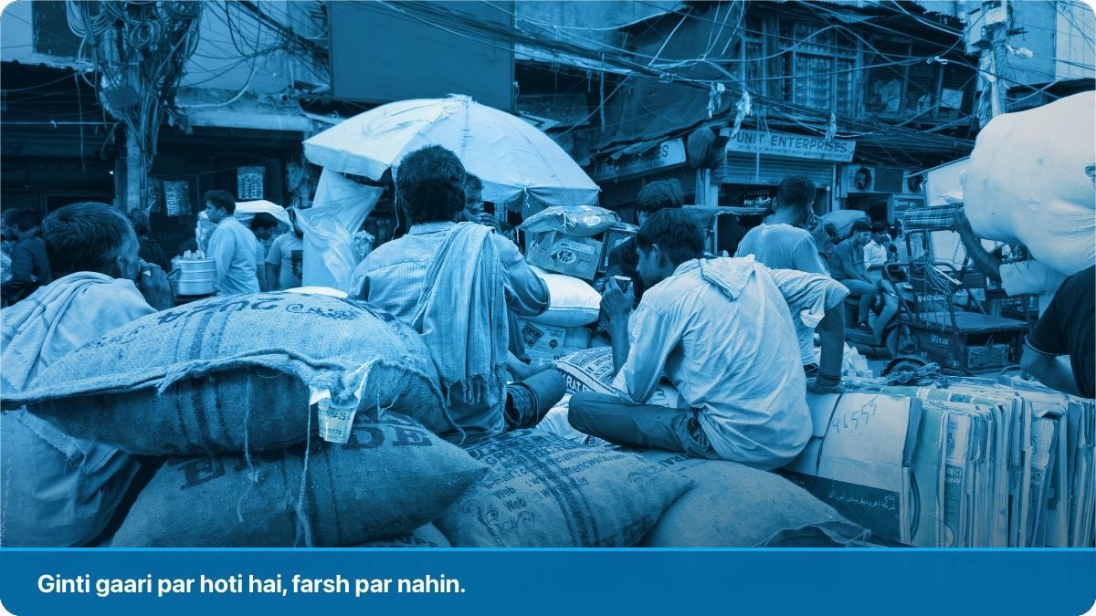 Bhare hue bazaar mein boron aur cartons se ladi rehri par mazdoor sustatay hue.