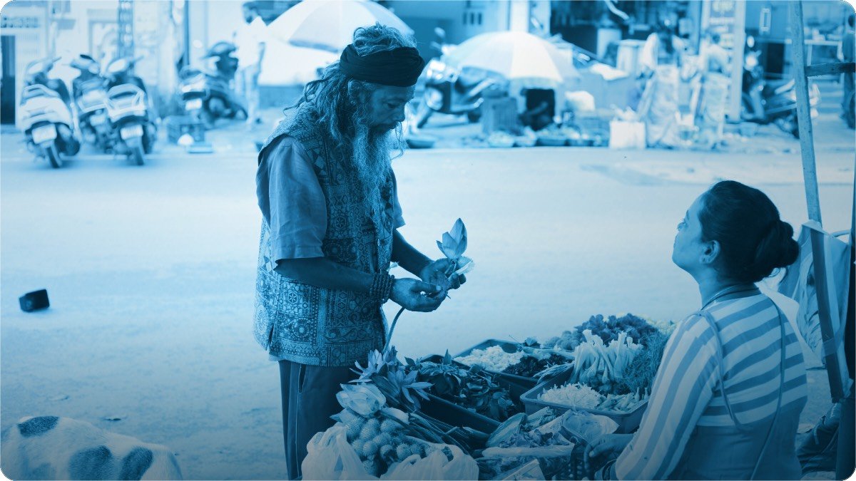 A street vendor serves a customer at her market stall on a busy Indian roadside in the afternoon.