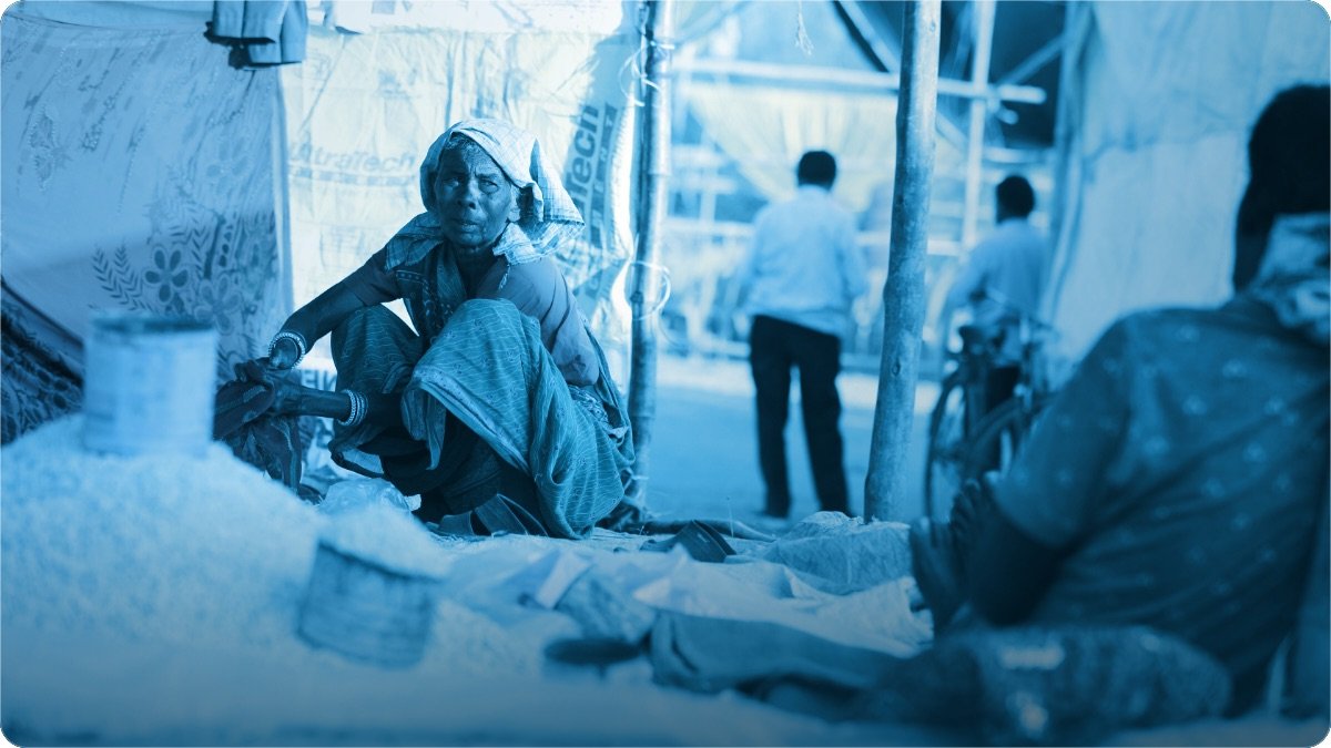 Haftawar bazaar mein tarpal ke neeche zameen par baithi dukandar, paas anaj ke dher lage hue.