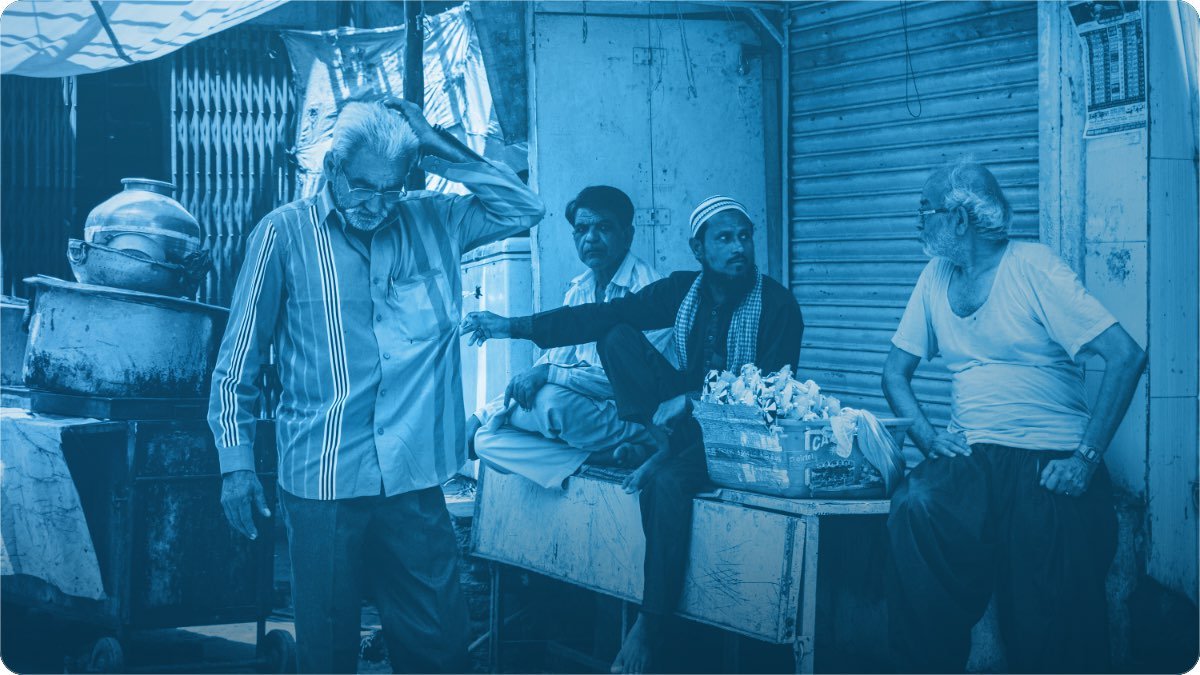 Four market men talking together beside their stalls, with shop shutters behind them.