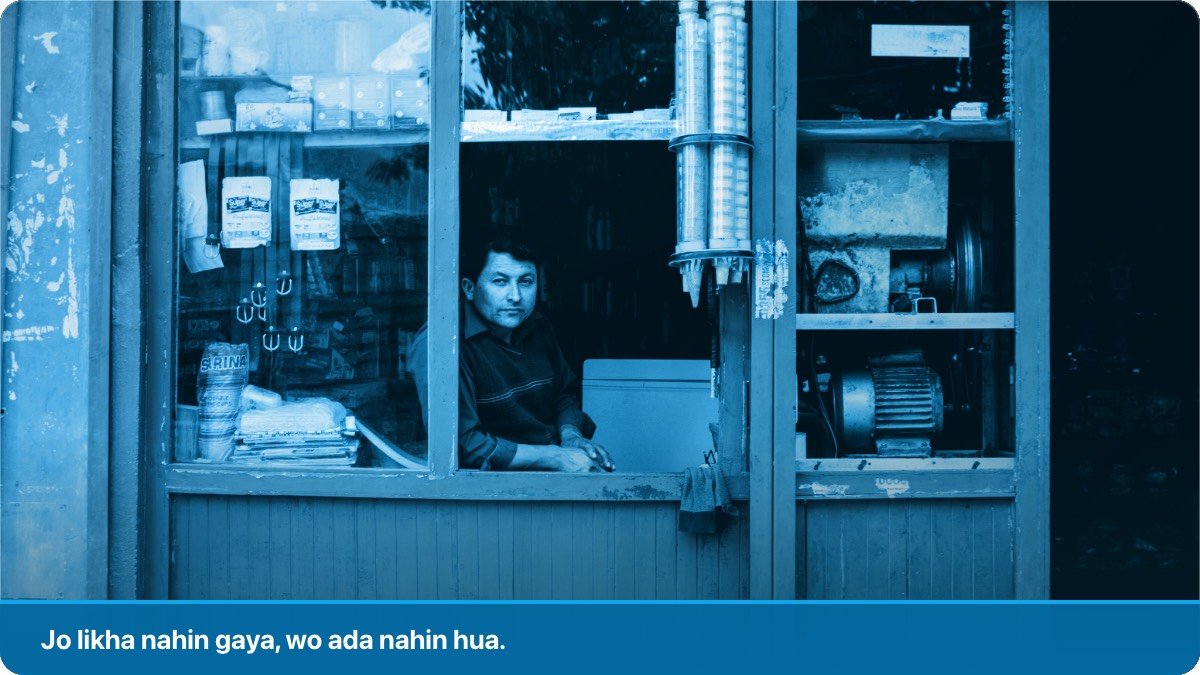 Apni chhoti si sarak kinare dukan ki khirki par baitha dukandar, peeche shelf par saman laga hua.