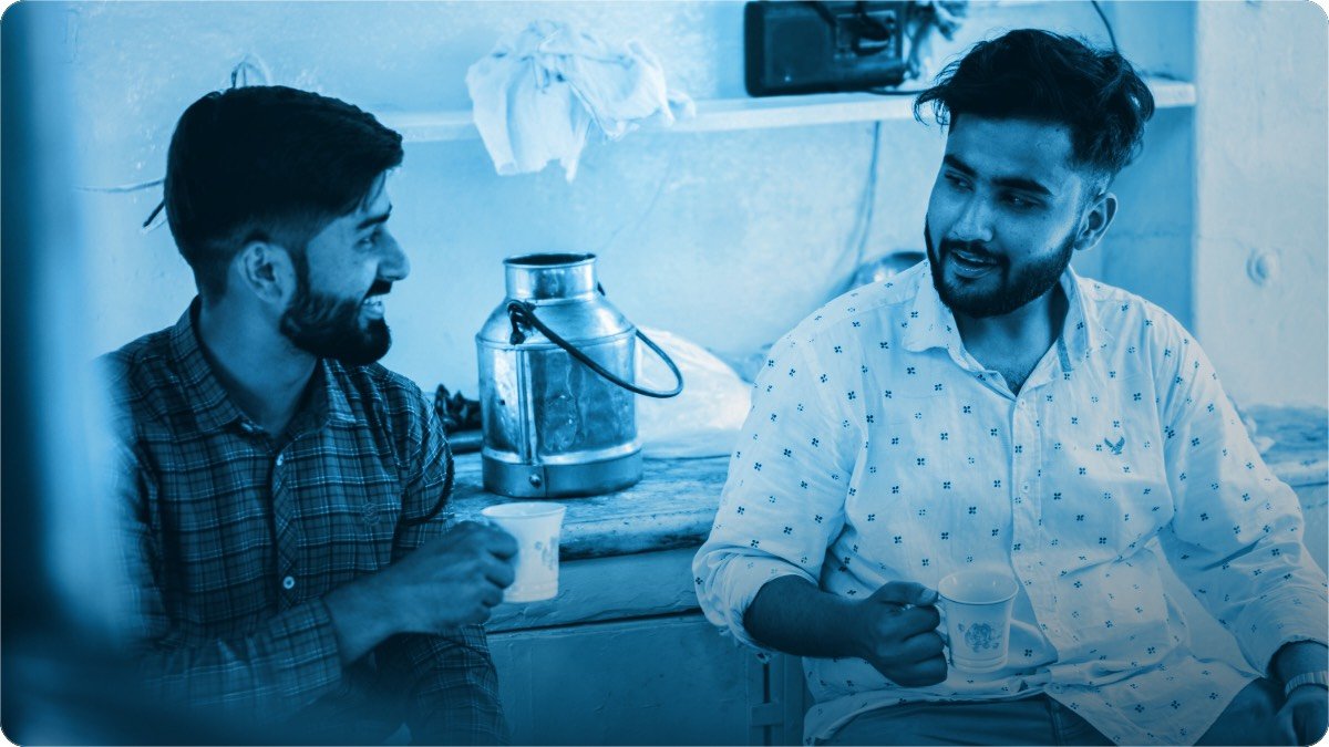 Two young men sitting with cups of tea in a small shop, in the middle of a serious conversation.