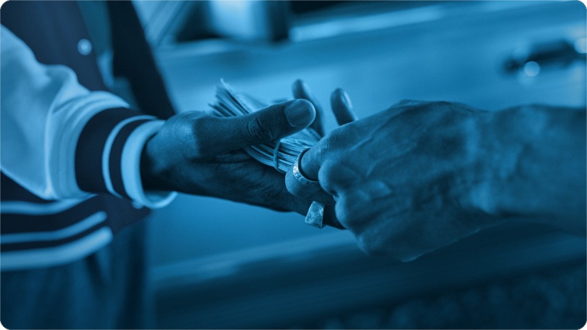 One hand passing a folded bundle of banknotes into an older person's open hand.